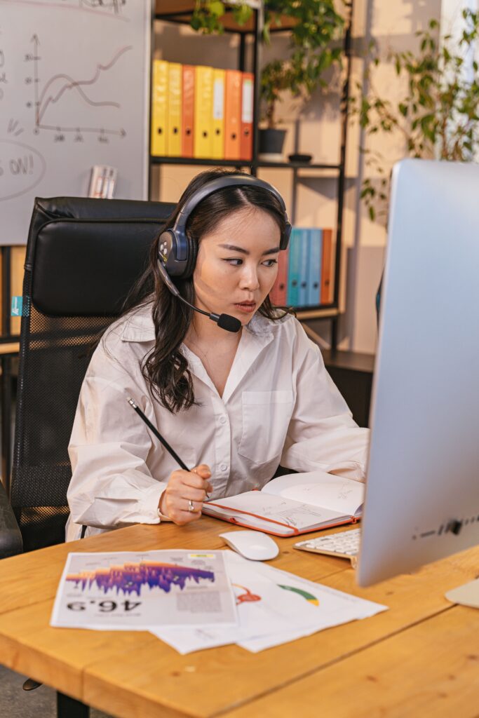 Businesswoman wearing headset, focused on computer work in modern office setting.
